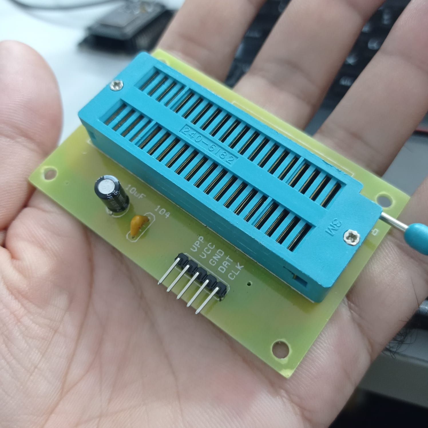 DS30F2010 Programming Socket For Pickit 3 Pickit 2 - a green PCB with a blue ZIF socket, a 5-pin header, and two capacitors held in a hand.