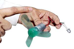 Dynamo Motor For LED - Unleash Power Of DIY Electricity Generator - a hand holding a small DC motor with a green three-blade plastic propeller attached and a clear LED connected via wires.