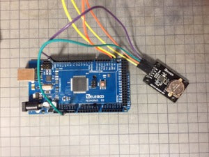 Elegoo DS1307 Module V03 - connected via multi-coloured jumper wires to a blue Elegoo Mega 2560 microcontroller board on a grid surface.