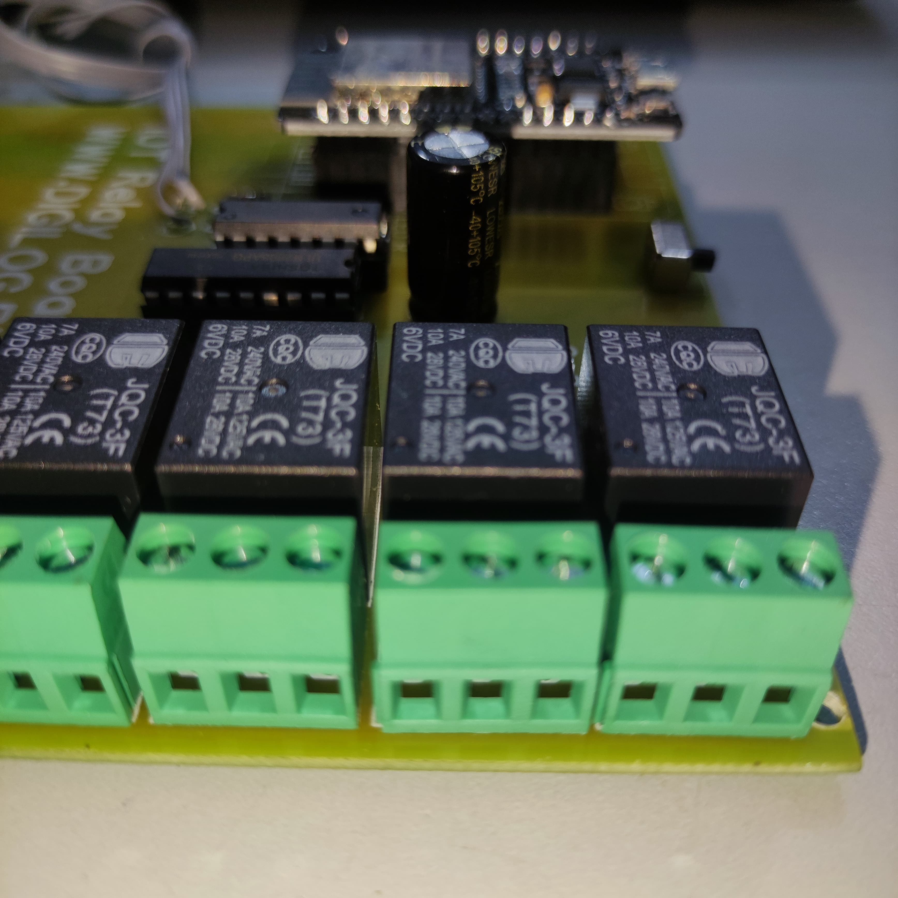 ESP32 Based 8 Channel Relay Board Micro Controller Board WiFi LAN Bluetooth - close-up of a green circuit board featuring four black JQC-3F relays, green screw terminals, and a central capacitor.