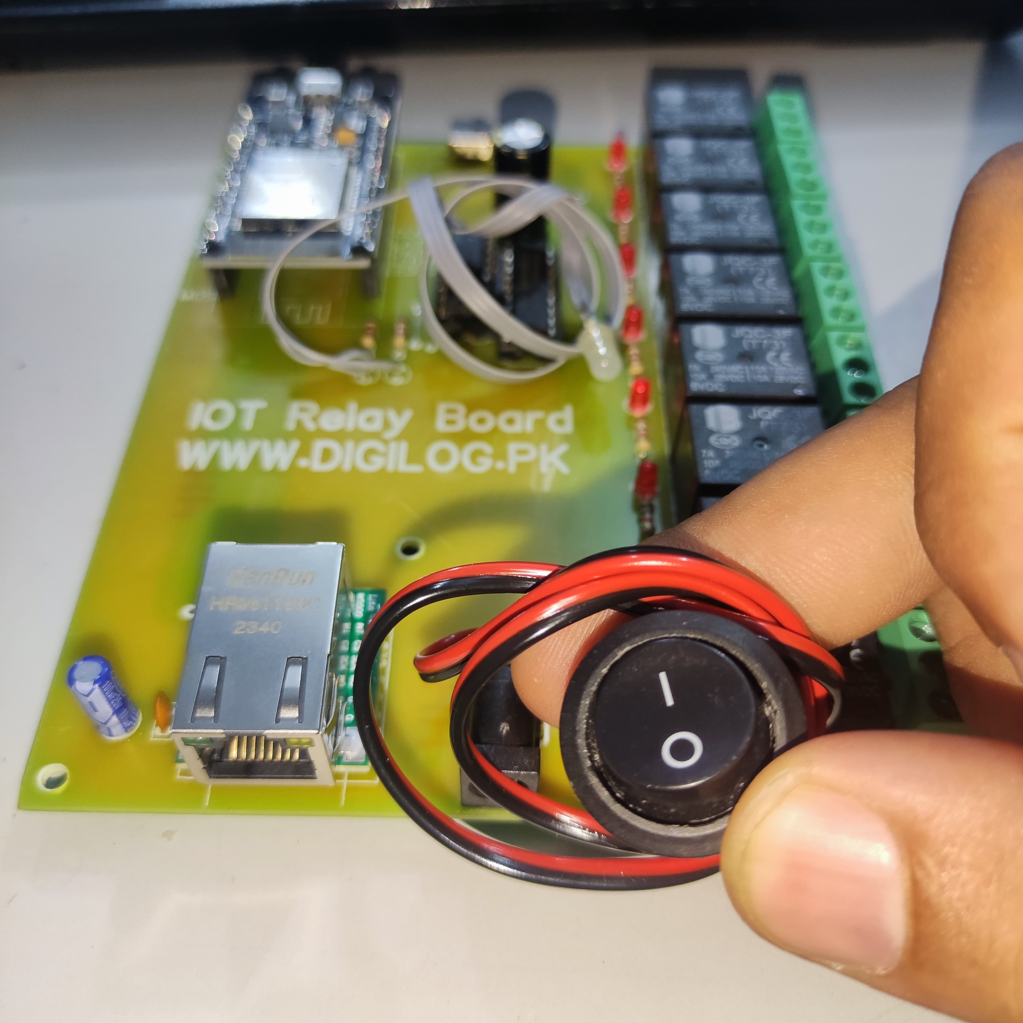 ESP32 Based 8 Channel Relay Board Micro Controller Board WiFi LAN Bluetooth - a green PCB with an Ethernet port, relays, and a hand holding a black circular rocker switch with wires.