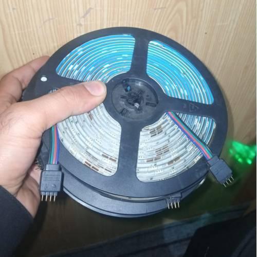 Faulty RGB LED Strip Lot 5 Meter 5 Meter 30 LED Per Meter Dusty Lot - a coiled strip of LED lights with a four-pin connector held in a hand.