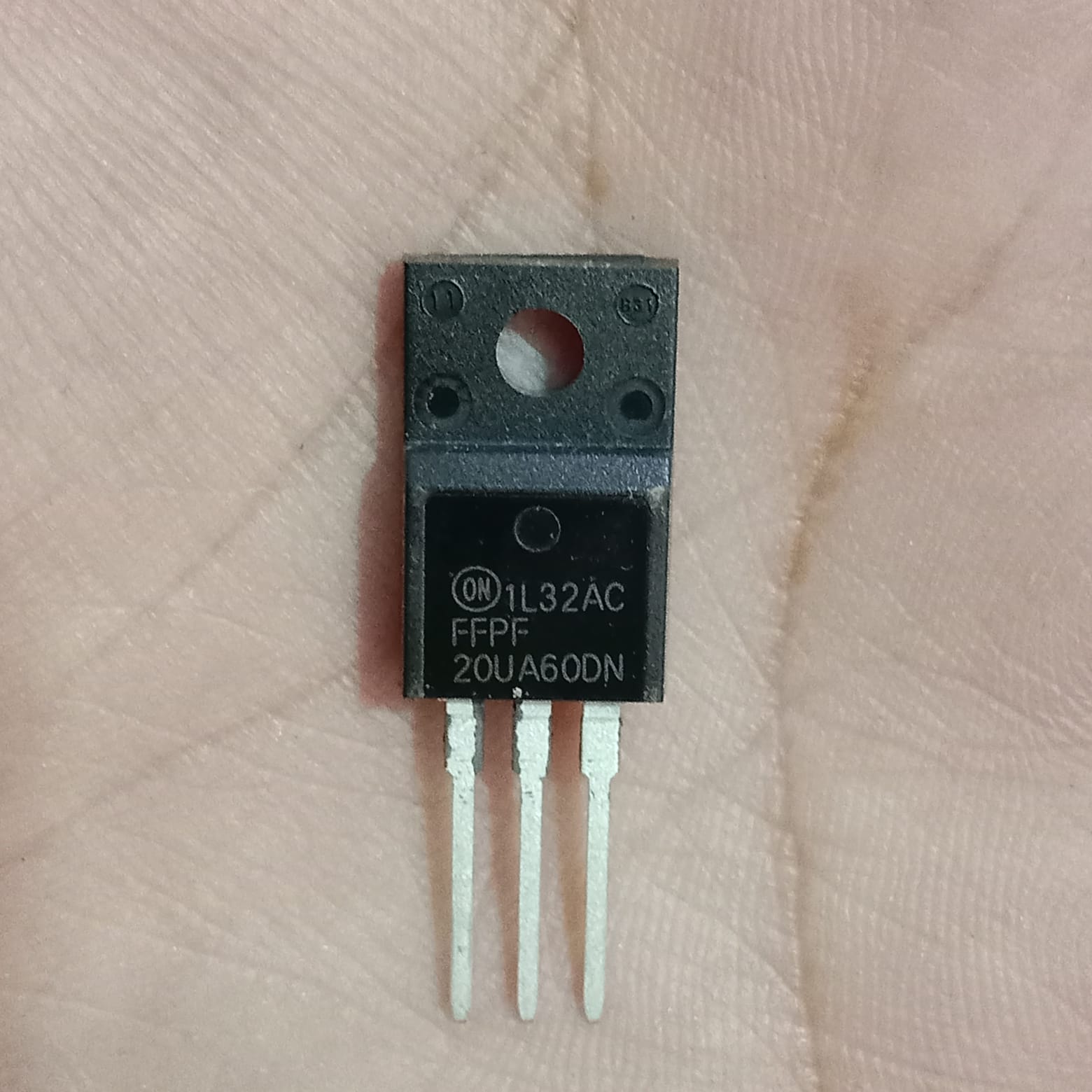 FFPF20UA60DN 600V 20A Ultrafast Dual Diode - a black, three-pin electronic component with a mounting hole, held against a person's palm.