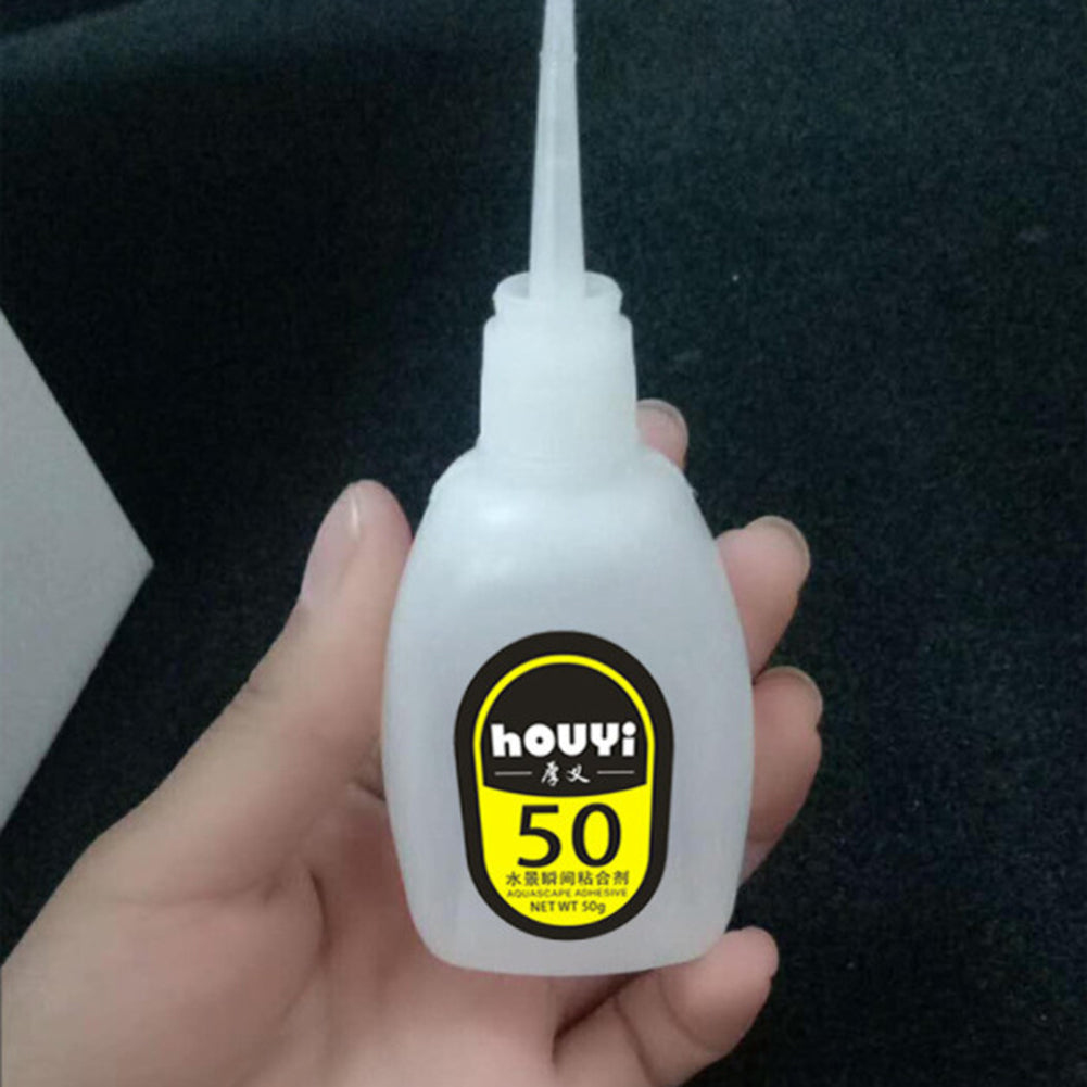 Gr 50G Fast-drying Glue Strong Adhesive Safe Non-toxic Glue Aquarium Landscape Supplies - a white plastic squeeze bottle with a pointed nozzle, held in a hand, featuring a yellow label with "houyi" and "50" text.