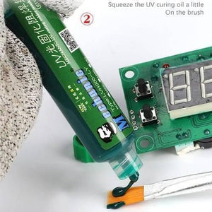 Green Mechanic UV Curable 10CC Solder Mask Ink PCB Fixing Repairing Welding Oil Paint Prevent Corrosive Arcing - tube dispensing oil onto a brush next to a green circuit board with two black buttons and a digital display.