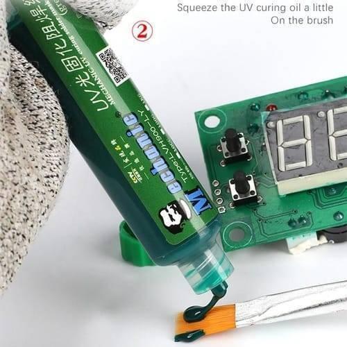 Green Mechanic UV Curable 10CC Solder Mask Ink PCB Fixing Repairing Welding Oil Paint Prevent Corrosive Arcing - tube dispensing oil onto a brush next to a green circuit board with two black buttons and a digital display.