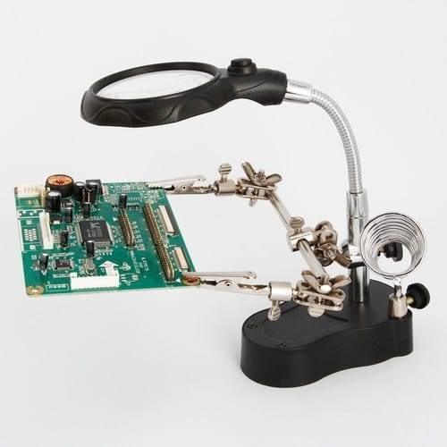 Helping Hand Clip Desktop LED Light Magnifier Glass With Soldering Stand 3.5x 12x - holds a green circuit board with two metal clips on a black base.