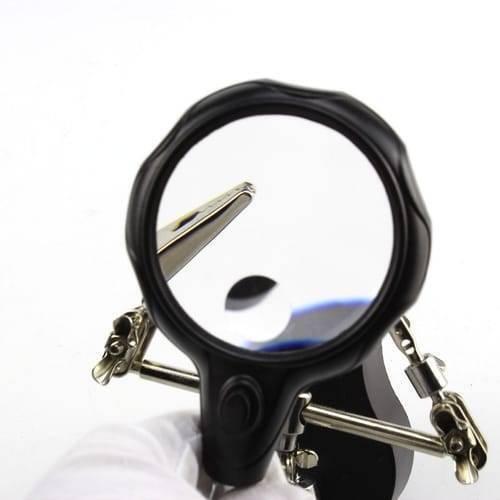 Helping Hand Clip Desktop LED Light Magnifier Glass With Soldering Stand 3.5x 12x - a black magnifying lens with a power button held by a gloved hand.