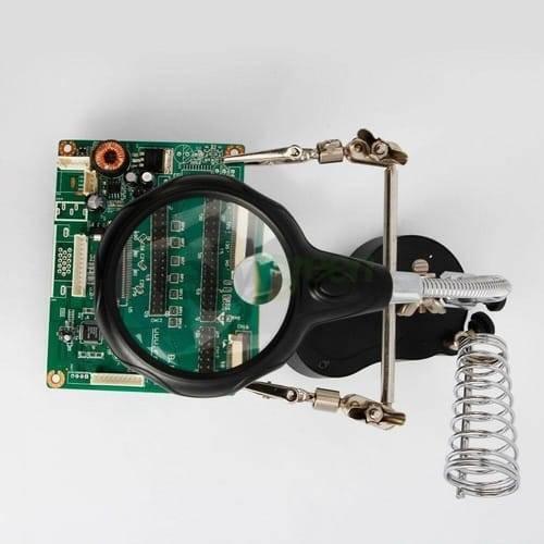 Helping Hand Clip Desktop LED Light Magnifier Glass With Soldering Stand 3.5x 12x - a green circuit board held by two alligator clips under a lens.