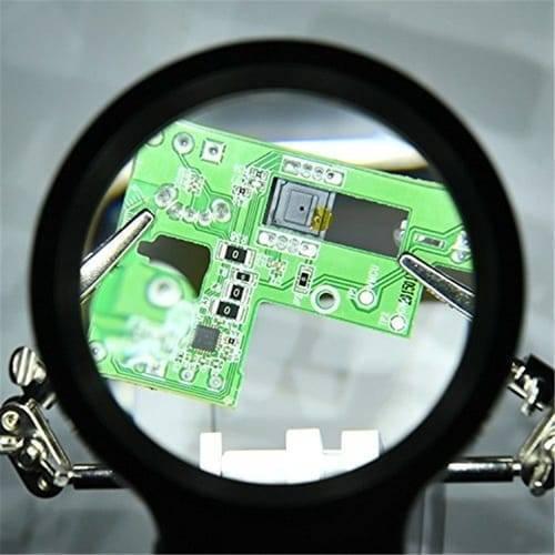 Helping Hand Clip Desktop LED Light Magnifier Glass With Soldering Stand 3.5x 12x - a green circuit board held by metal clips under a magnifying lens.