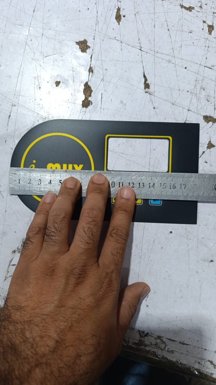 Hybride LCD Sticker Idm-7 Sticker For Graphical LCD Based Local Solar Inverter - a black rectangular panel with a yellow circular logo and a rectangular cutout, being measured with a metal ruler.