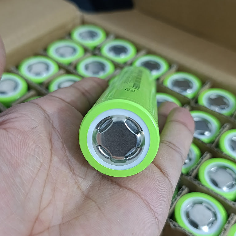IFR32140 LiFePO4 Battery Cell 3.2V 15Ah 15A - Grade A Fresh Stock - a close-up of a single lime-green cylindrical cell held in a hand with a box of identical cells in the background.