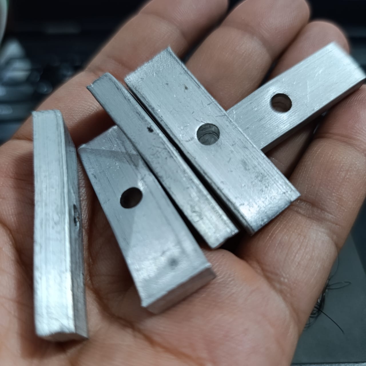 IGBT Fitting - a set of four rectangular silver-coloured metal mounting bars, each featuring a single circular hole, held in a person's hand.