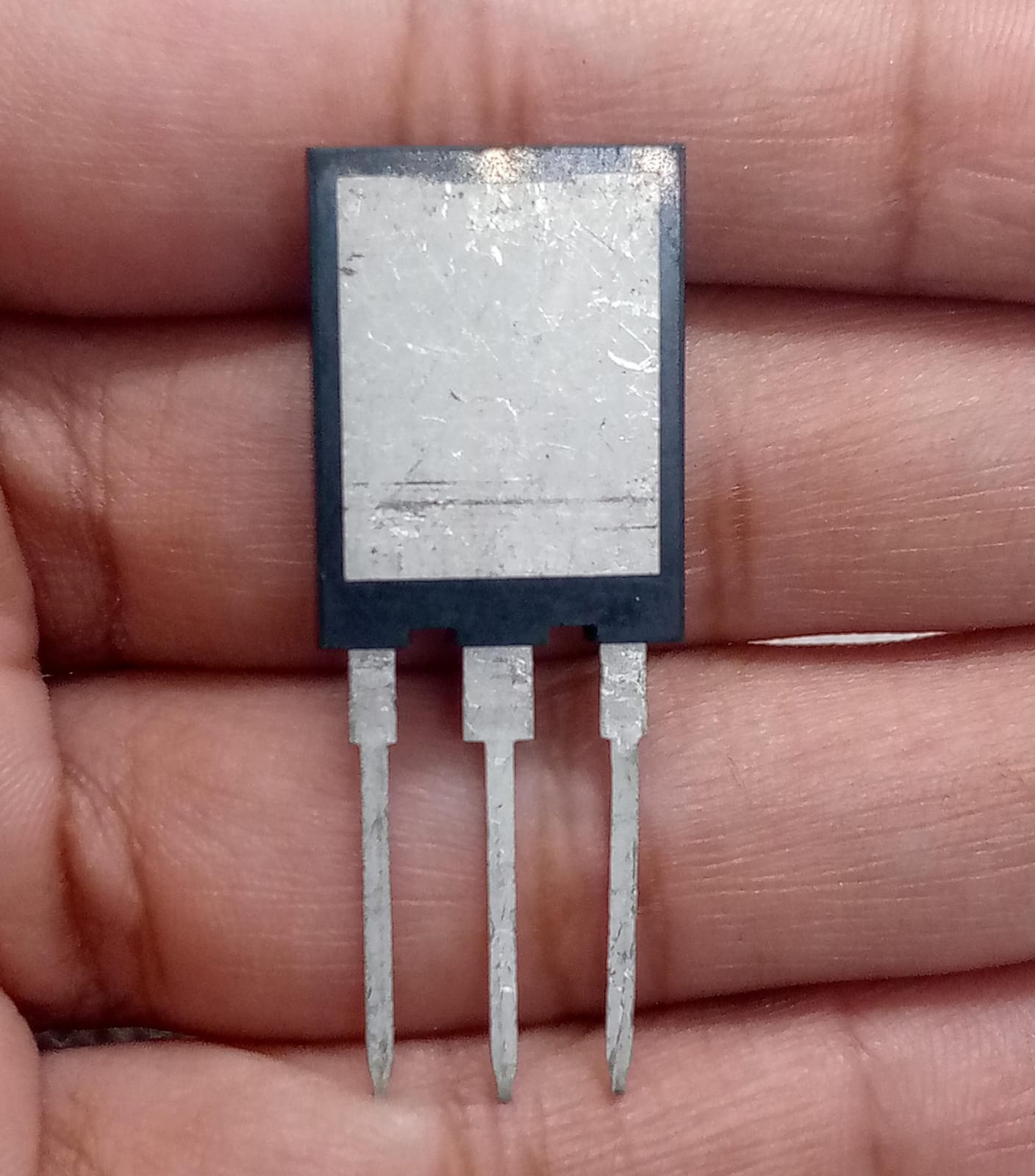 IGBT P75V120FDB2 - a close-up view of a black three-pin electronic component with a silver metal heat sink plate held between fingers.
