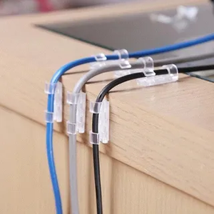 Clear adhesive cable clips holding blue, white, and black cables along a desk edge