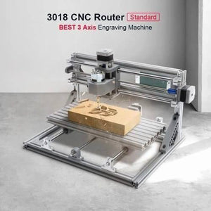 Imported CNC Engraving PCB Milling Machine Wood Carving CNC 3018 - a silver metal 3-axis engraving machine shown carving a Transformers logo into a rectangular wooden block on its platform.