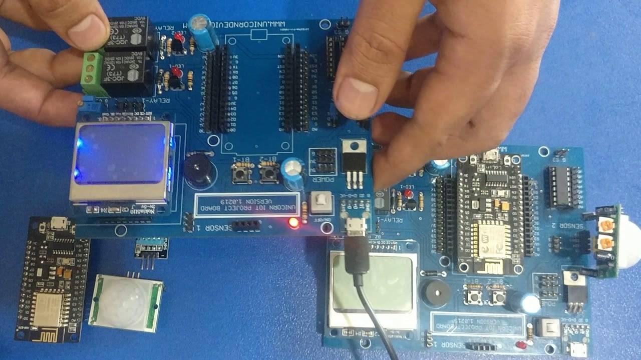 IOT Project Board PCB - two blue circuit boards with displays, relays, buttons, and a USB power cable being held by hands.