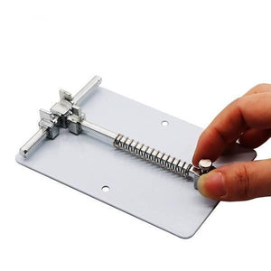 Jakemy Mobile Phone Motherboard Circuit PCB Board Holder Clamp Stand JM-Z15 - a hand adjusting the spring-loaded metal clamp on a white base plate.