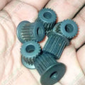 Japanese 30 Teeth 6.35mm Bore GT3 Timing Pulley P30 Push Fit Type - a close-up of several dark grey, multi-toothed cylindrical pulleys in a hand.