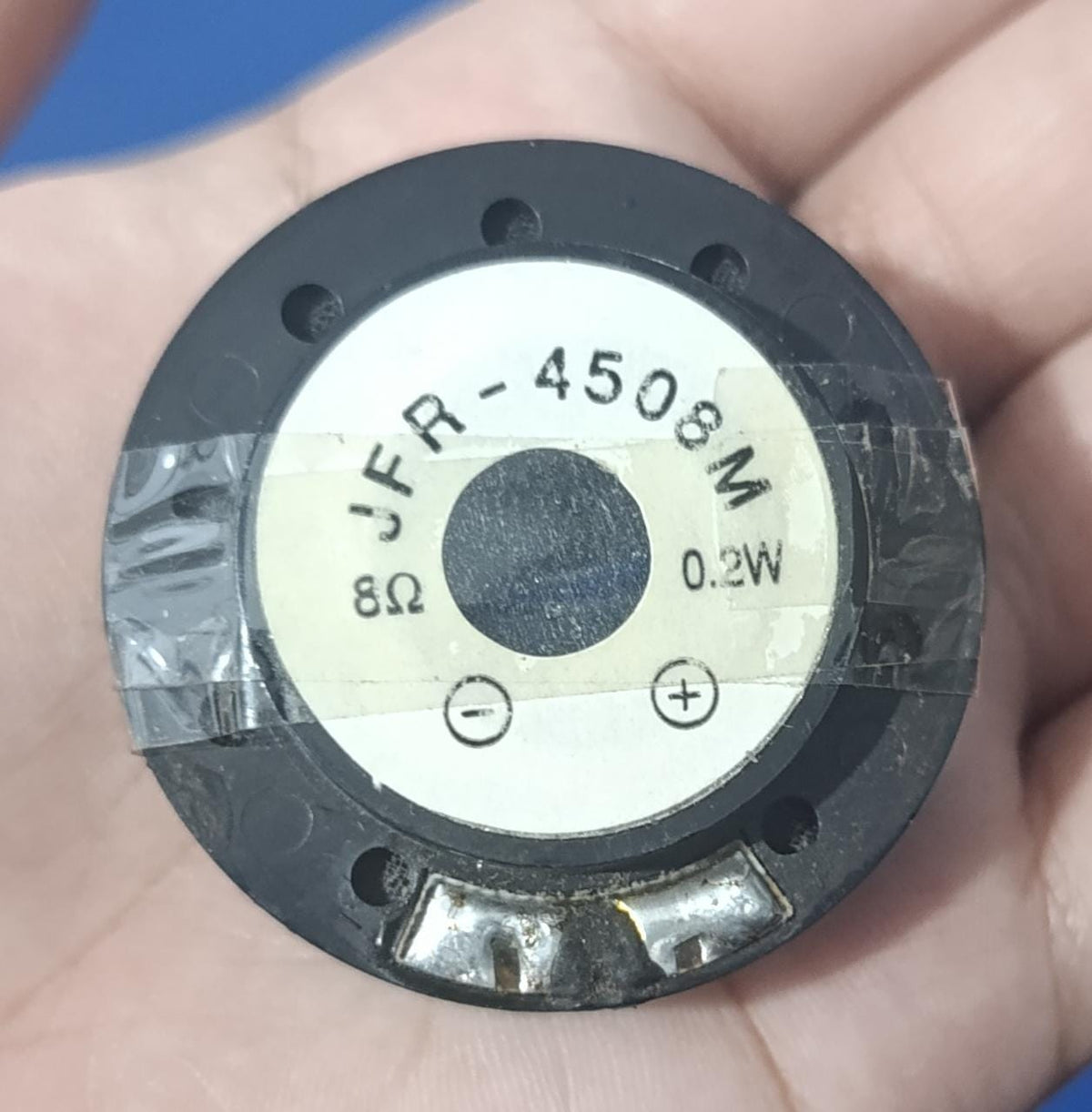 JFR-4508M 8Ω 0.2W Mini Speaker - a circular black component with a white label showing the model number, impedance, power rating, and polarity symbols.