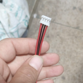 JST2.0 2mm Pitch 4 Pin Connector Wire - a close-up showing a white four-pin connector attached to red and black ribbon wires held by a hand.