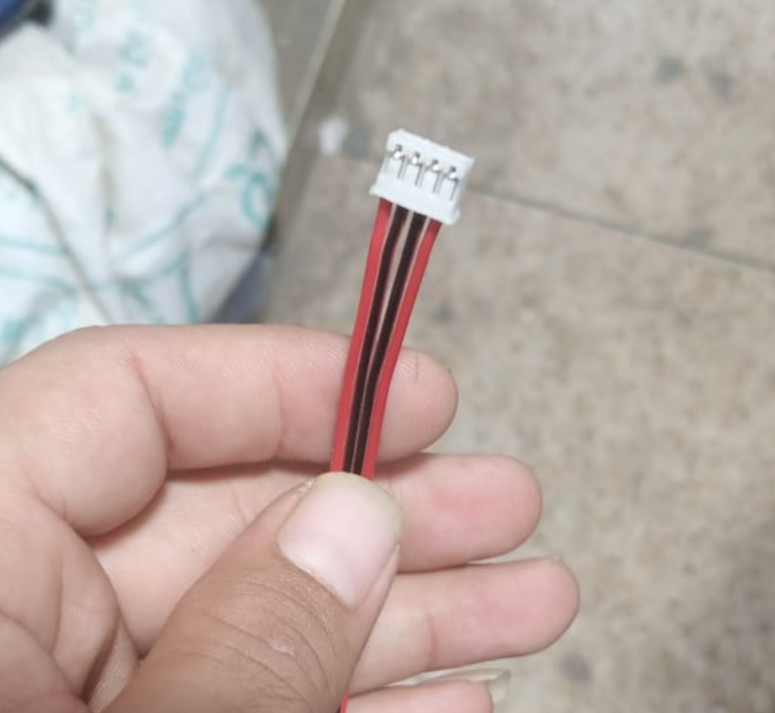 JST2.0 2mm Pitch 4 Pin Connector Wire - a close-up showing a white four-pin connector attached to red and black ribbon wires held by a hand.