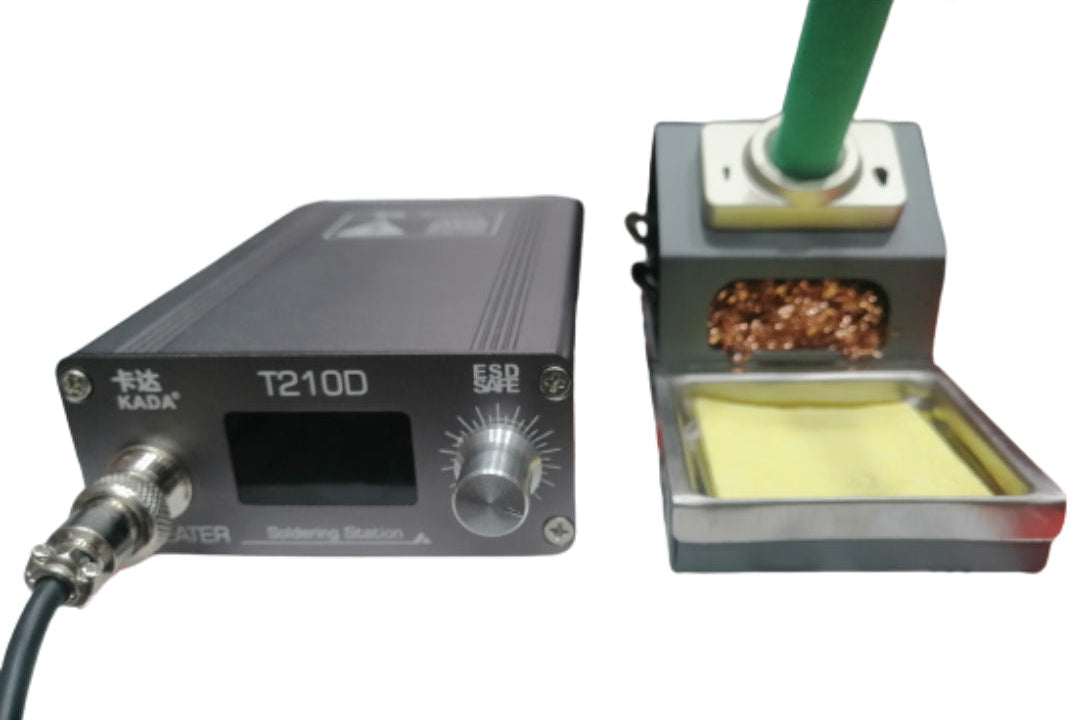 Kada T210D Thermostatic Soldering Station – 75W, Adjustable Temperature 120–450°c, LED Display, Auto Sleep, Pid Control - with a black control unit featuring a display and knob, next to a stand with a brass tip cleaner and yellow sponge.