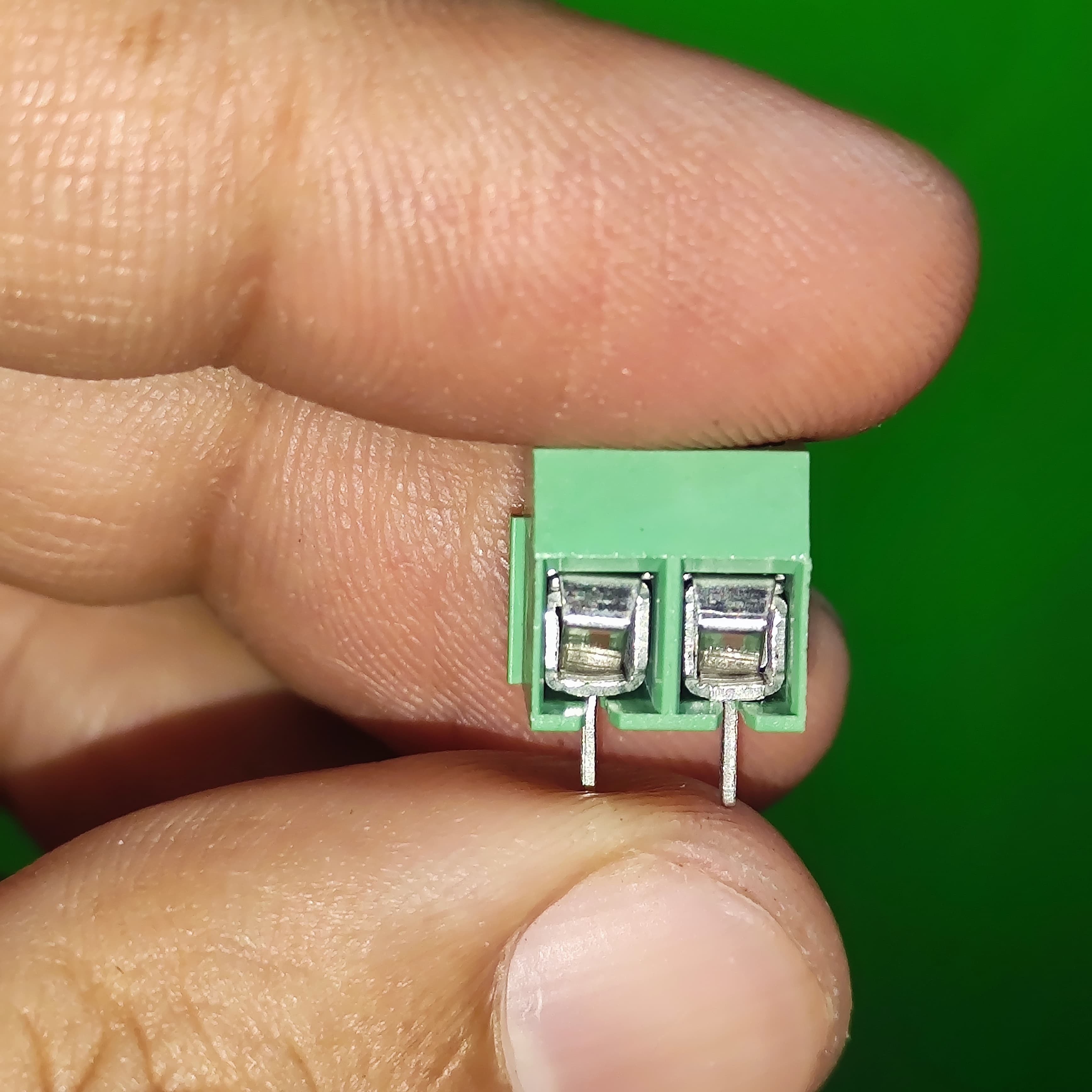 Kf 350 /kf 126 250V 10A 5mm Pitch Green Color 2 Pin Screw Terminal Connector Tblock - a close-up view held between fingers showing the green plastic housing and two metal wire entry ports.