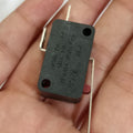 Limit switch - a small rectangular black electronic component with a red actuator button and three metal terminal pins, held in a person's hand.