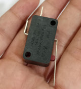 Limit switch - a small rectangular black electronic component with a red actuator button and three metal terminal pins, held in a person's hand.