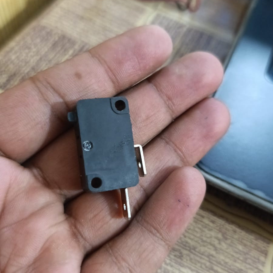 Limit switch - held in a palm, showing a small black rectangular housing with an actuator button on the side and two metal spade terminals.