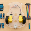 Line Following Robot 2wd With L298 - kit components laid out including an Arduino Uno, motor driver, chassis with wheels, sensors, battery holder, and wires.