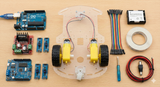 Line Following Robot 2wd With L298 - kit components laid out including an Arduino Uno, motor driver, chassis with wheels, sensors, battery holder, and wires.