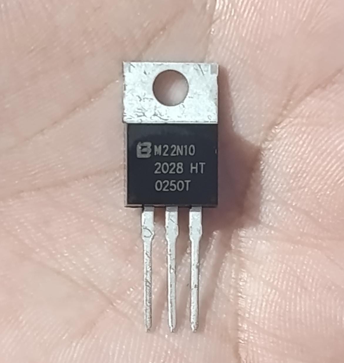 M22N10 100V 22A N-Channel Power MOSFET (TO-220) - a black TO-220 electronic component with three metal pins and a mounting hole, held in a hand with text printed on its surface.