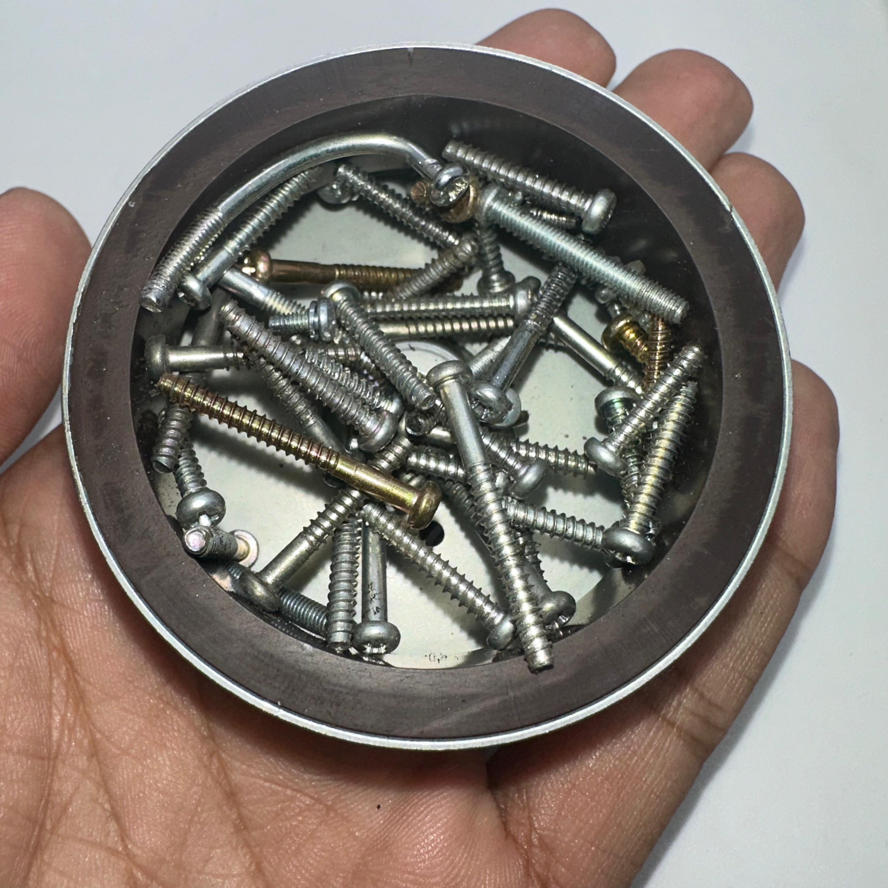 Magnet for storing screws and metal - a round silver-coloured magnetic bowl held in a hand and filled with various metal screws.