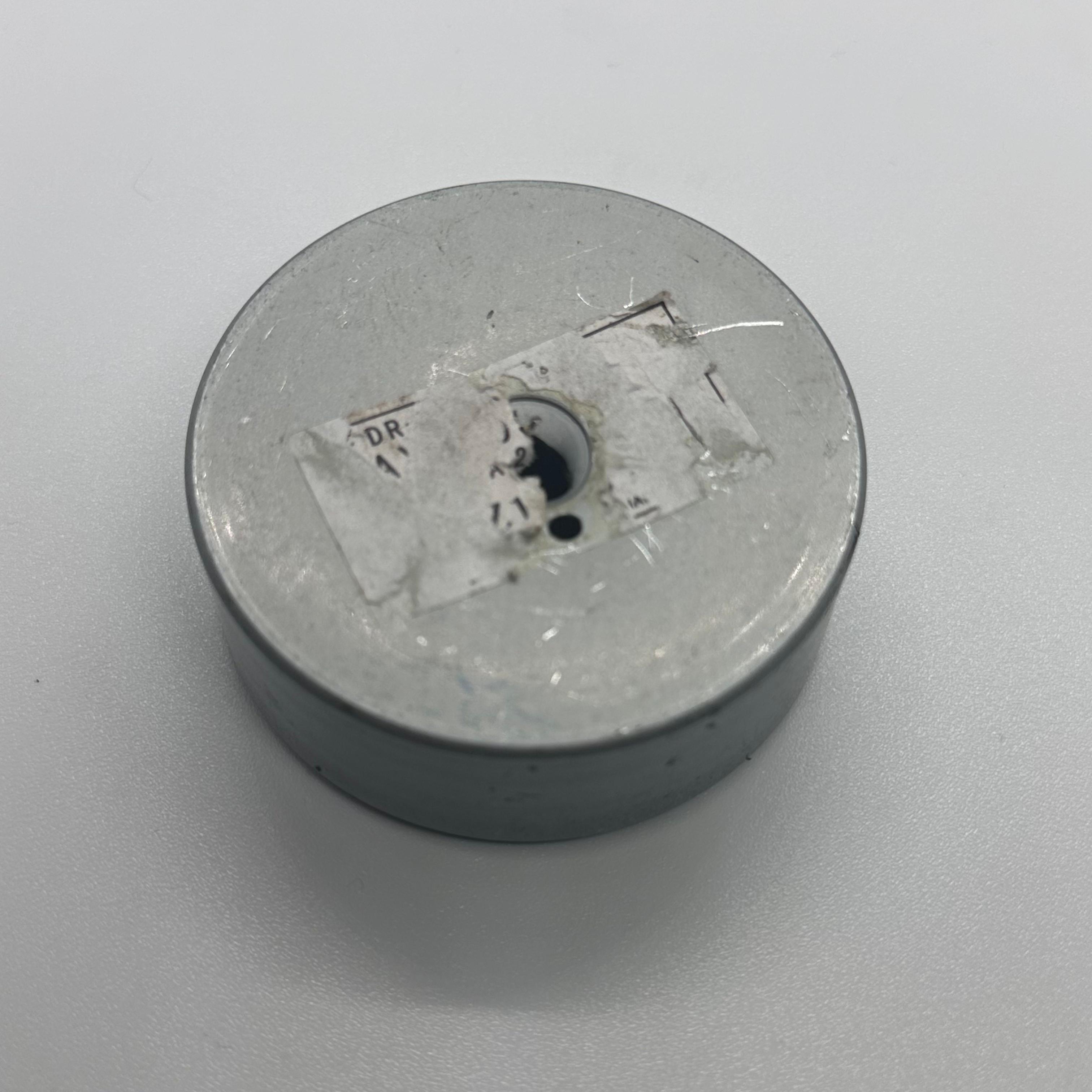 Magnet for storing screws and metal - a circular grey magnetic base with a central hole and a partially torn white label on the top surface.