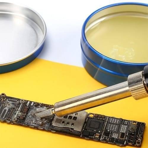 Mechanic Soldering Flux Paste PCB BGA Welding Flux Gel Tin MCN-UV50 - shown in a blue tin container with its lid nearby, while a soldering iron tip works on a small circuit board.