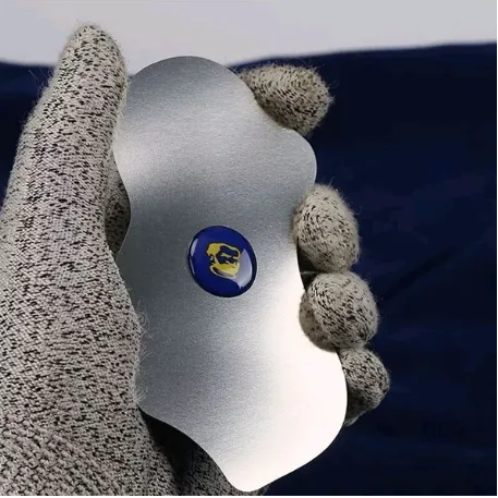 MECHANIC X9 OPENING TOOL - scalloped, metallic silver tool held by a gloved hand, featuring a central circular blue emblem with a stylized yellow face graphic.