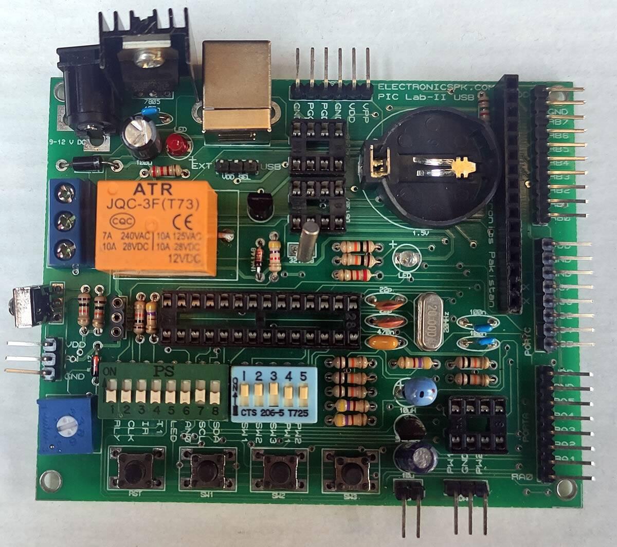 Microchip Pic Lab-ii Development Board 28 Pin Microcontrollers - a green circuit board with a 28-pin socket, orange relay, USB port, power jack, buttons, and dip switches.