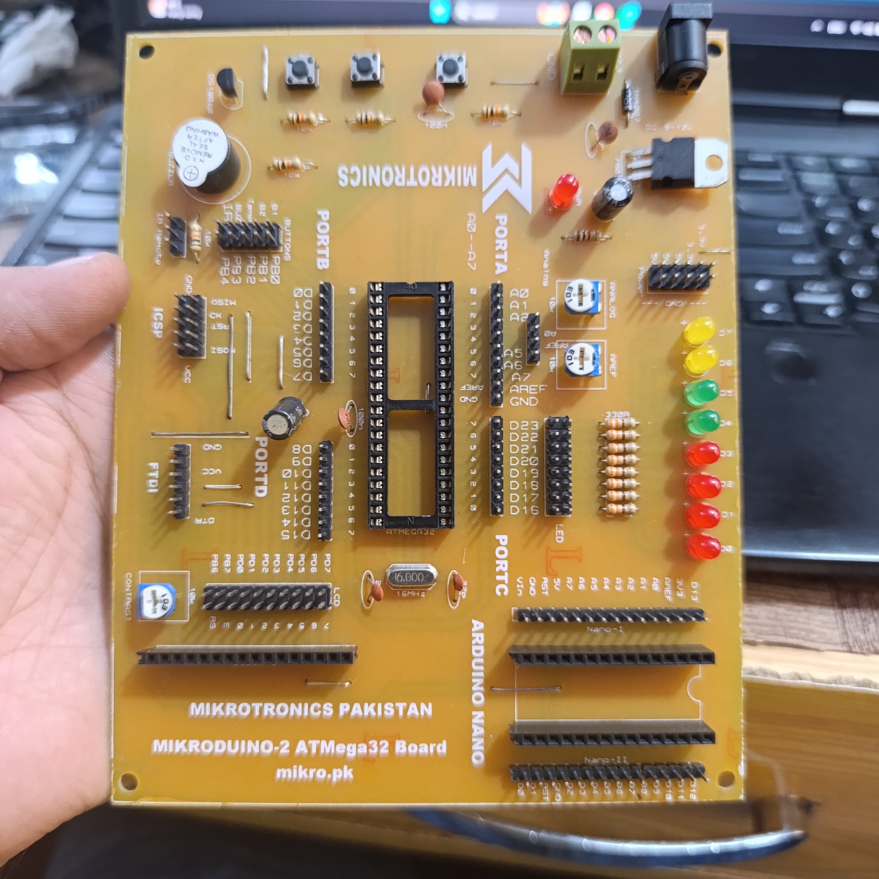 MikroDuino-II AVR ATMEGA32 Arduino Compatible Board Without LCD ,IC And Arduion - a yellow circuit board with a 40-pin IC socket, multiple pin headers, LED indicators, and buttons, held in a hand.