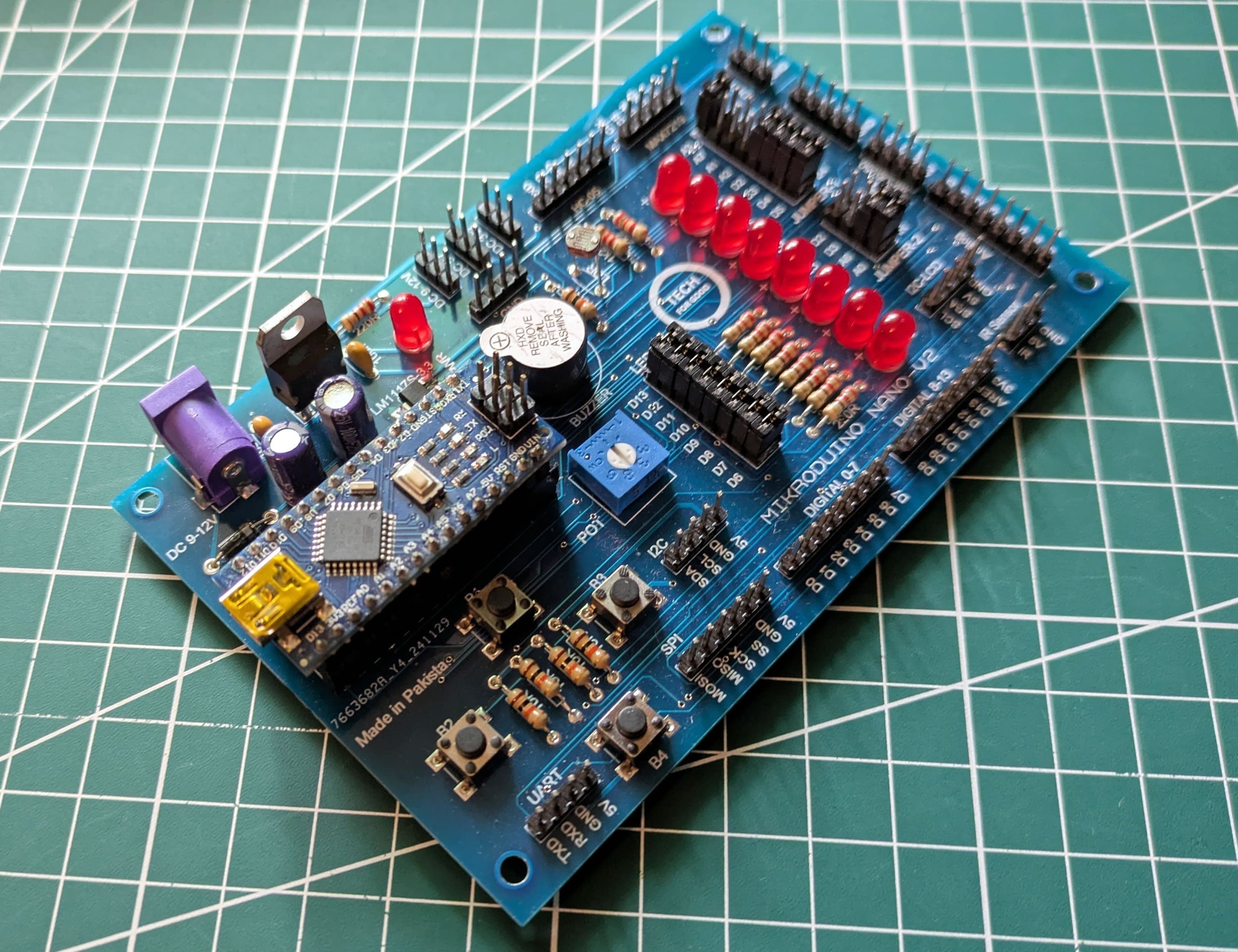 Mikroduino Nano — Arduino Nano Trainer Development Board And Learning Shield Board Made - with a blue PCB, featuring a mounted Arduino Nano, eight red LEDs, four push buttons, a buzzer, and a potentiometer.
