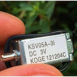Mini 3V DC Solenoid Valve KSV05A Normally Open For Gas Air Valve - a silver rectangular metal valve with a nozzle and two black wires, held between fingers.