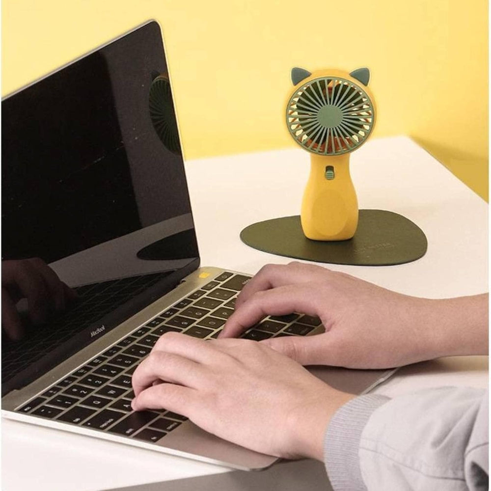Mini USB Rechargeable Small Handheld Fan | Portable Table Fan Wholesale - a yellow, cat-eared portable fan with a power button, standing on a dark base next to a laptop.