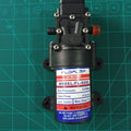 Mist Pump High Pressure Low Noise 12V 70W 4.5l/min Fog Maker Pump - a black 12V DC motor pump with two ports, shown against a green cutting mat.