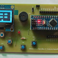 NanoBoy – The Arduino Gaming Console for Learning and Creativity - a green PCB with a blue OLED screen displaying a game, a buzzer, an LED, six push buttons, and a Nano board.