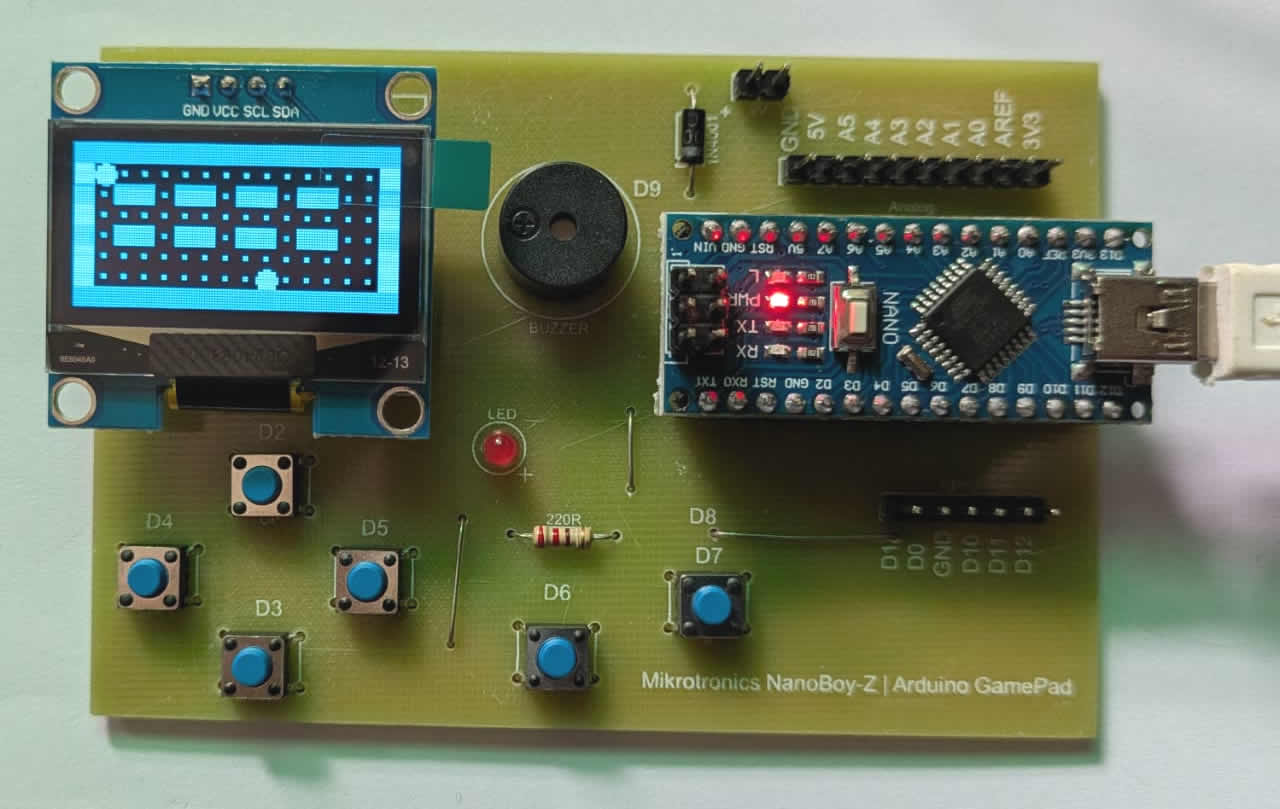 NanoBoy – The Arduino Gaming Console for Learning and Creativity - a green PCB with a blue OLED screen displaying a game, a buzzer, an LED, six push buttons, and a Nano board.