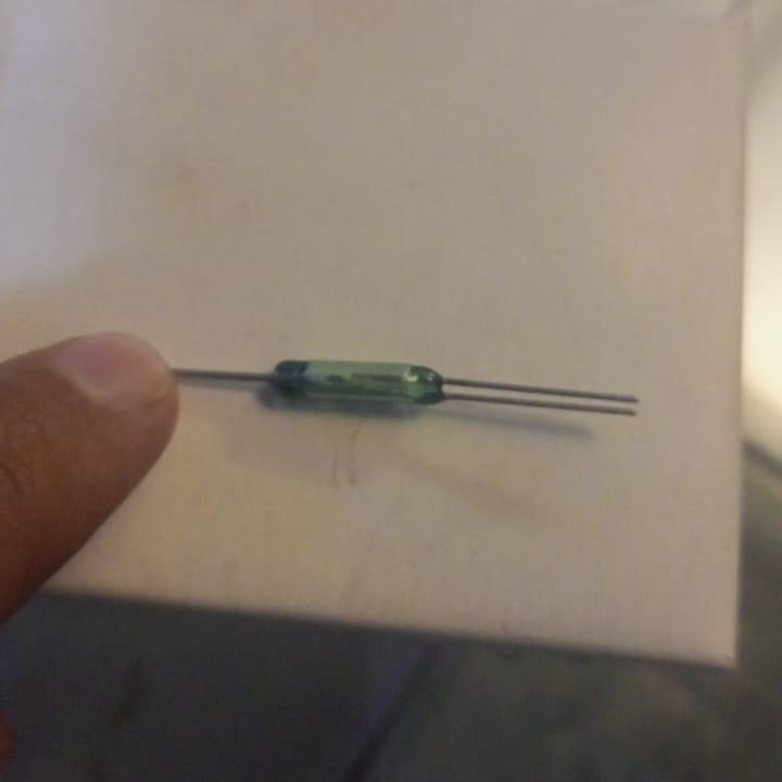 NC NO 3-Wire Reed Switch Sensor - a close-up of a glass-encased reed switch with one lead on one end and two leads on the other held by a finger.