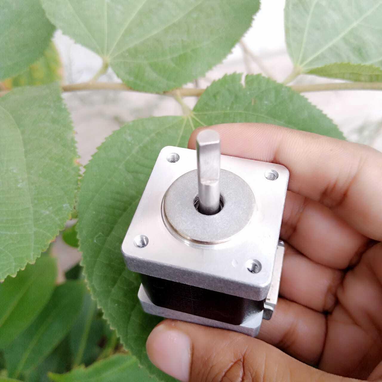 NEMA 11 stepper motor without connector - a close-up of the silver square mounting face and the central metal shaft held in a hand.