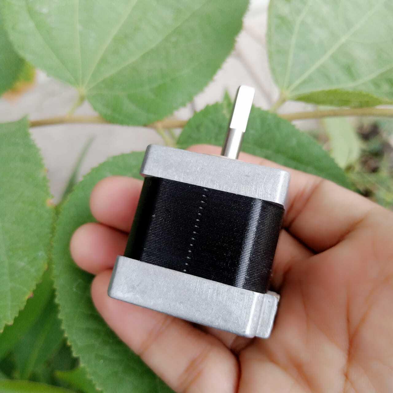 NEMA 11 stepper motor without connector - shown held in a hand, featuring a square silver metal frame with a black central body and a single protruding metal shaft.