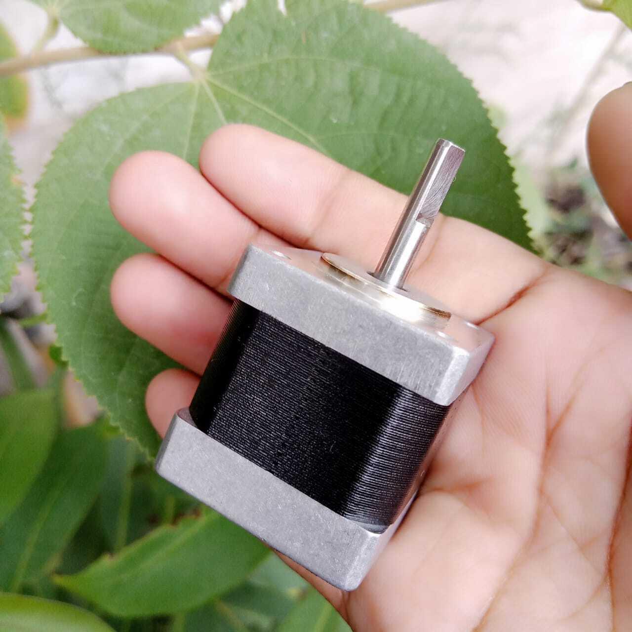 NEMA 11 stepper motor without connector - shown held in a hand, featuring a square silver metal body with a black central section and a single protruding metal shaft.